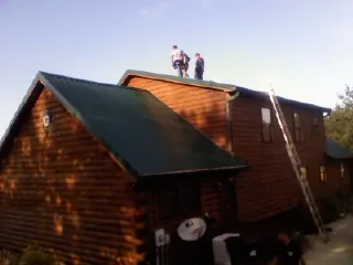 Crew on the ridge of a green metal roof on a two story log home in Seymour