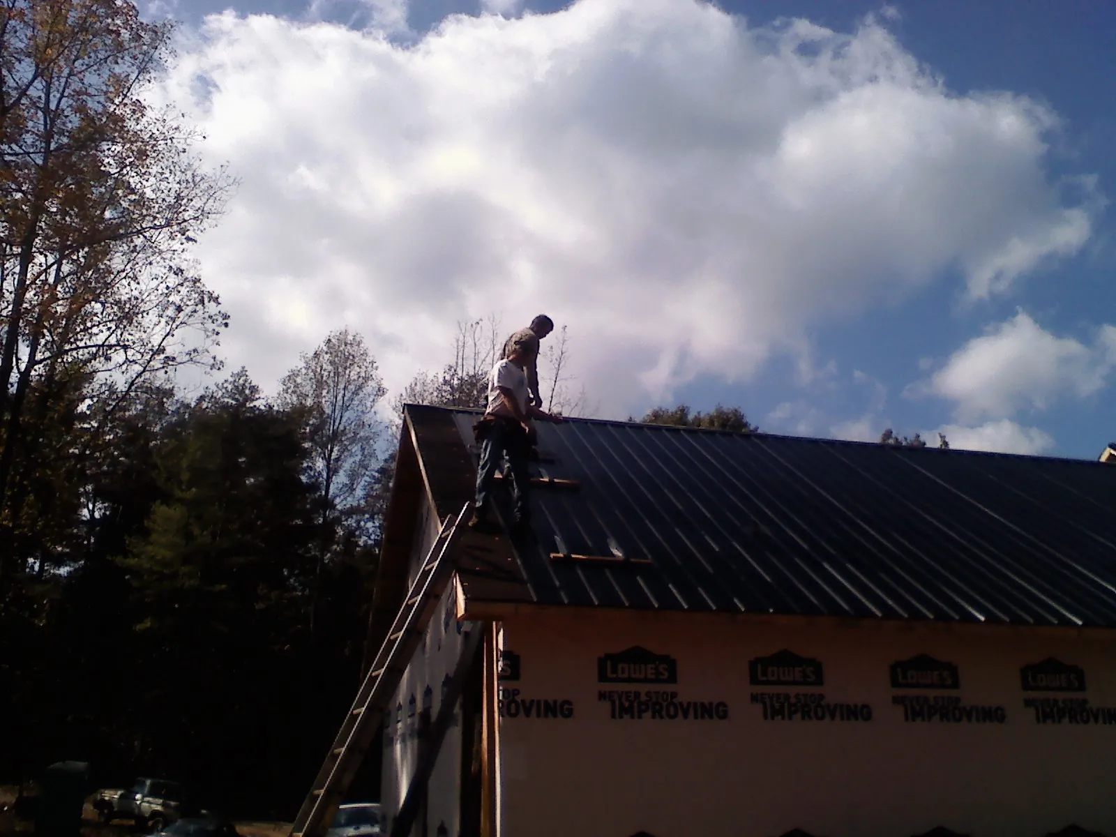 Roofer fastening dark metal panels high against a cloudy sky, from a Roof Inspection job in Seymour